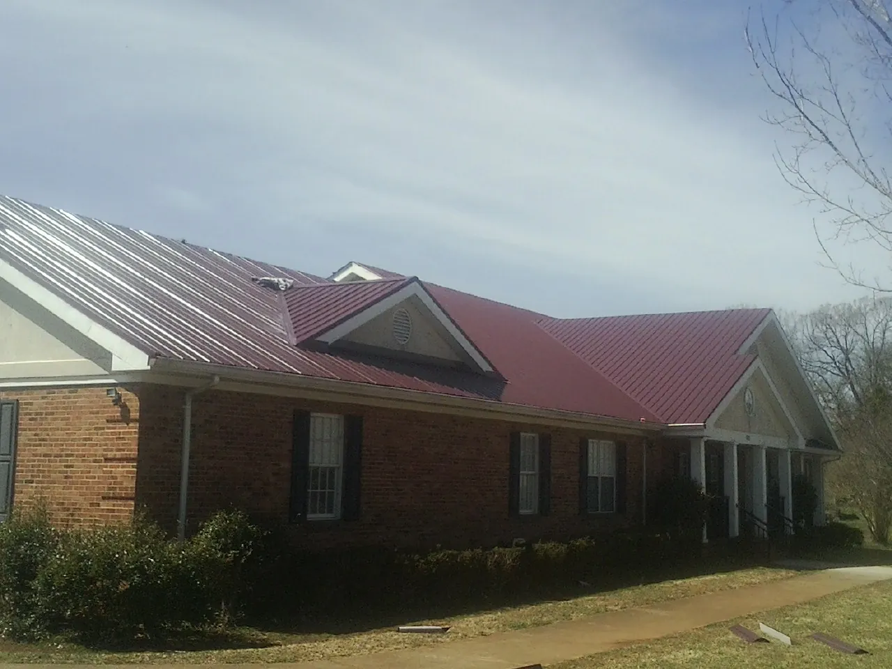 Red metal roof with gabled entries on a long brick building, from a Hail Damage Roof Repair job in South Amboy