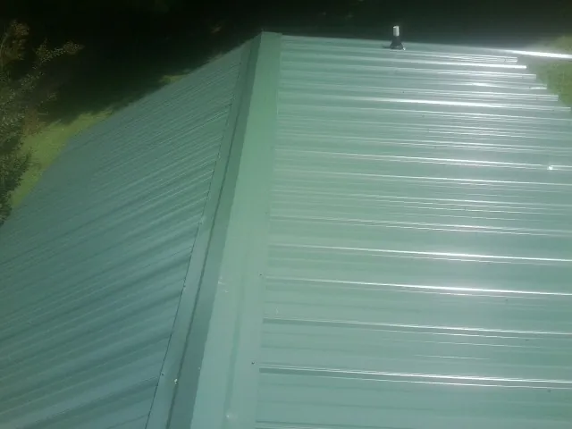 New green metal panels meeting at the ridge of a roof — Flat Roof Repair work by our crew in South Amboy