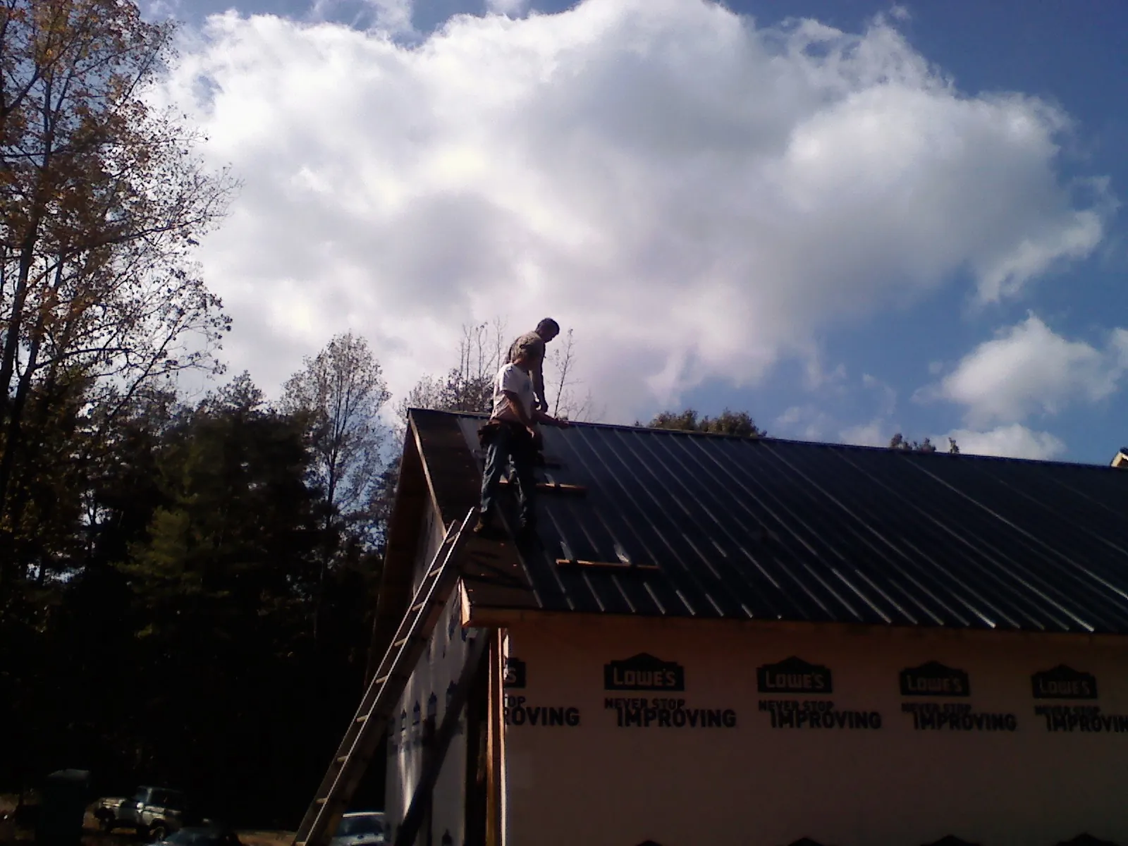 Roofer fastening dark metal panels high against a cloudy sky, from a Roof Inspection job in South Amboy