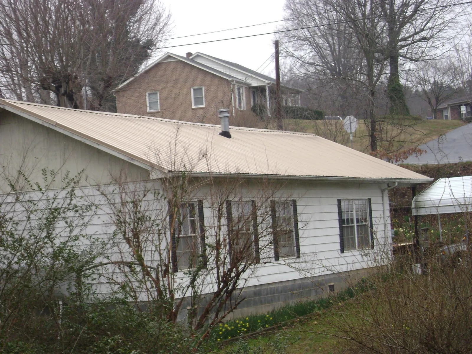 Tan metal roof on a white sided house set into a hillside — Commercial Roofing by Roofing Brothers in South Amboy